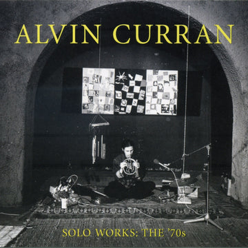 CD cover featuring a black and white photograph of Alvin Curran seated at a keyboard in front of a checkered backdrop. The text on the cover reads 'Alvin Curran Solo Works: The '70s'.