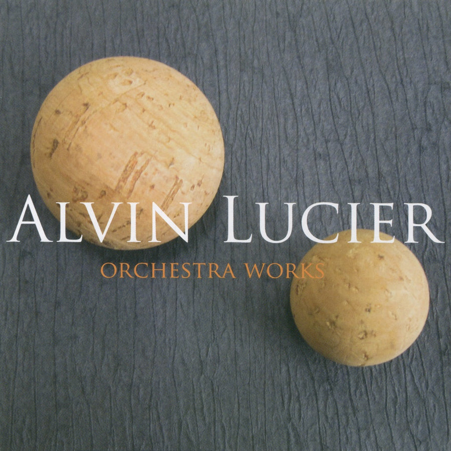 Cover of the album 'Alvin Lucier: Orchestra Works' featuring two light-colored, possibly wooden spheres on a dark textured background, with the artist and album title text.
